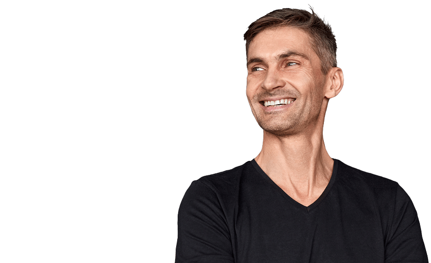 A man with short brown hair wearing a black V-neck shirt smiles while looking to his left against a plain, light background.
