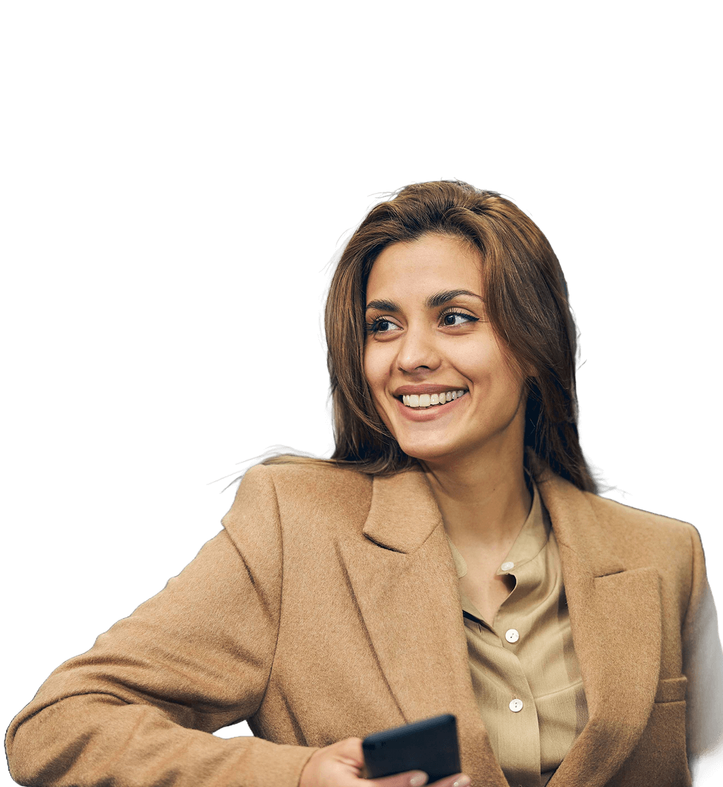 Woman in a tan blazer smiling and holding a smartphone, looking to the side against a plain light background.